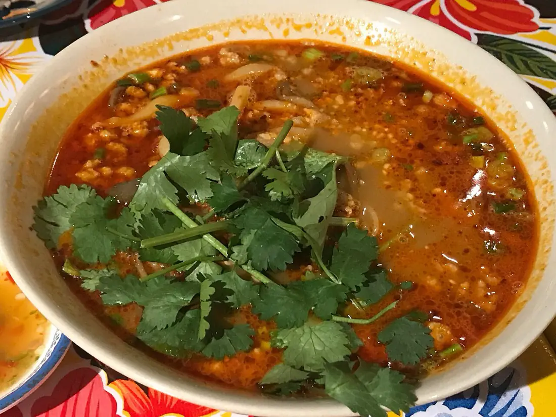 A bowl of tom yam kung, scattered with herbs and chilli